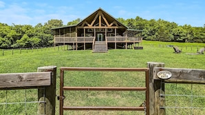 A wooden cabin with a balcony, surrounded by a grassy field and trees.