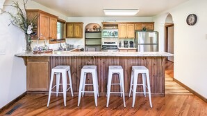 A modern kitchen with wooden cabinets, a central island with bar stools, stainless steel appliances, and a clock on the wall.