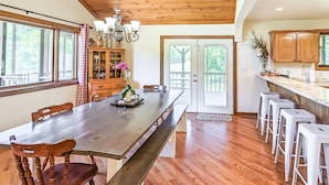 A spacious kitchen with a long wooden table, white bar stools, and a wooden cabinet.