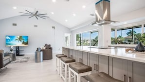 A modern kitchen with a large island, bar stools, and a view of the outdoors. - Luxury Modern Waterfront 3BR Villa for 8, Heated Pool, Walk to Beach, Top Dining (Marco Island)