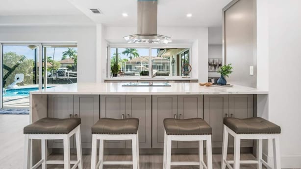 A modern kitchen with a large island, bar stools, and a view of a swimming pool. - Luxury Modern Waterfront 3BR Villa for 8, Heated Pool, Walk to Beach, Top Dining (Marco Island)