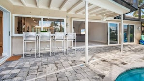 A covered patio area with a pool, featuring a seating arrangement with chairs and a table. - Luxury Modern Waterfront 3BR Villa for 8, Heated Pool, Walk to Beach, Top Dining (Marco Island)