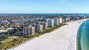 A coastal cityscape with high-rise buildings, a wide sandy beach, and a clear blue ocean. - Luxury Modern Waterfront 3BR Villa for 8, Heated Pool, Walk to Beach, Top Dining (Marco Island)