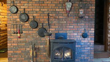 A rustic wooden interior with a brick fireplace, hanging cookware, and a lantern.