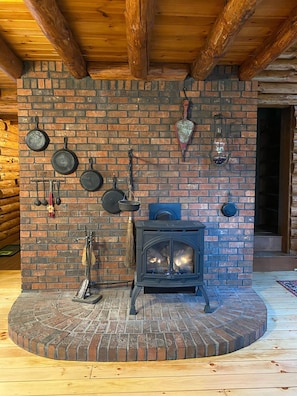 Un intérieur rustique en bois, avec une cheminée en briques, des ustensiles de cuisine suspendus et une lanterne.