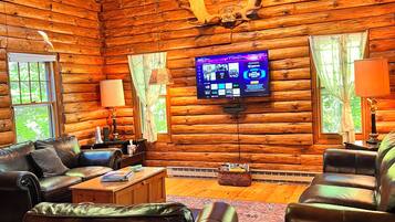 L’intérieur d’une cabane en rondins, avec une cheminée, des canapés en cuir, un téléviseur à écran plat et une décoration rustique.