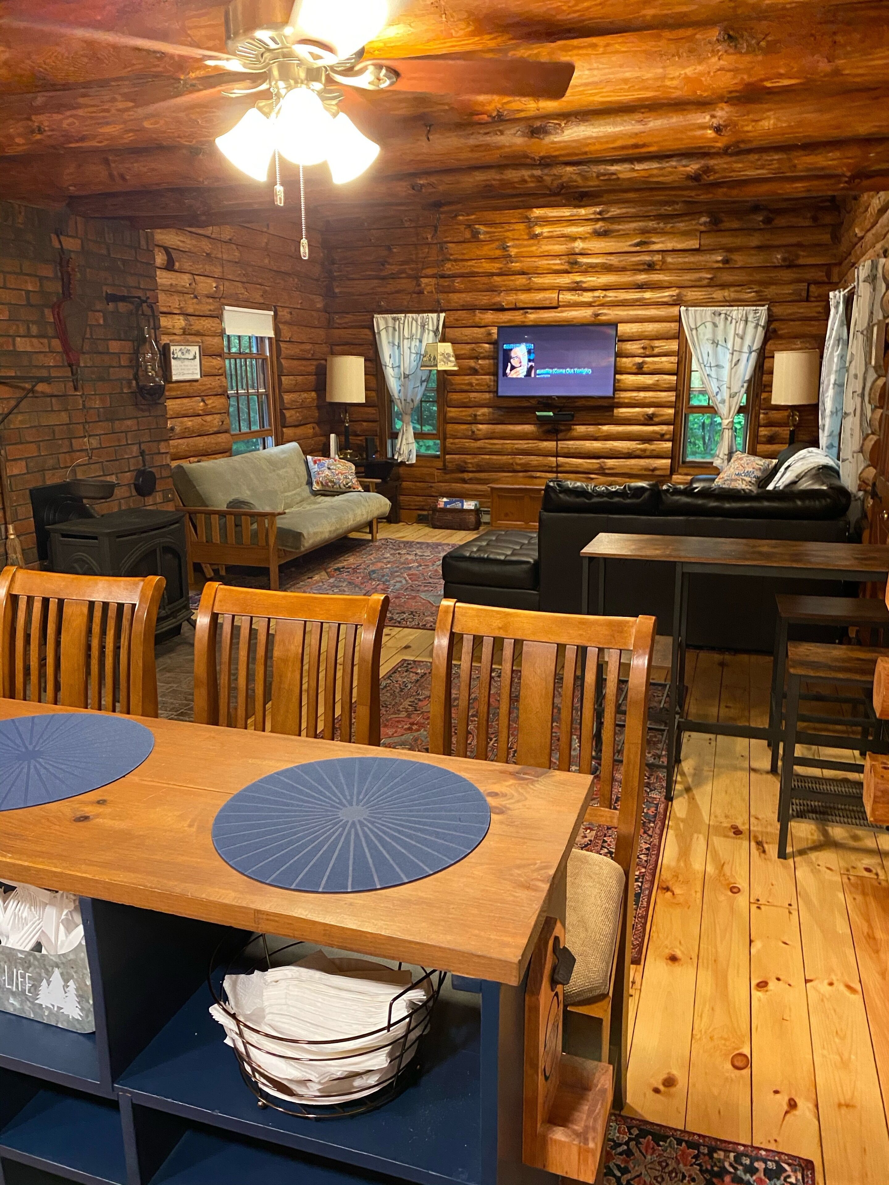 Een gezellig blokhut interieur met een houten eettafel, stoelen, een bank en een aan de muur bevestigde televisie.