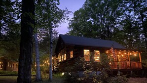A log cabin with a porch, surrounded by trees.