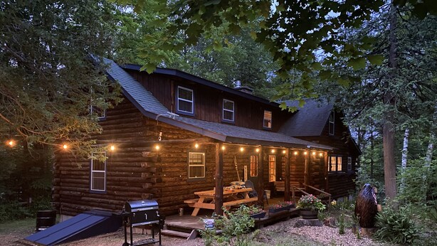 A log cabin with a porch, a barbecue grill, and a picnic table.