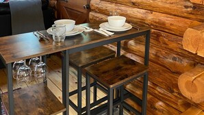 A rustic wooden cabin interior with a dining table set for two, a bench, and a poster on the wall.
