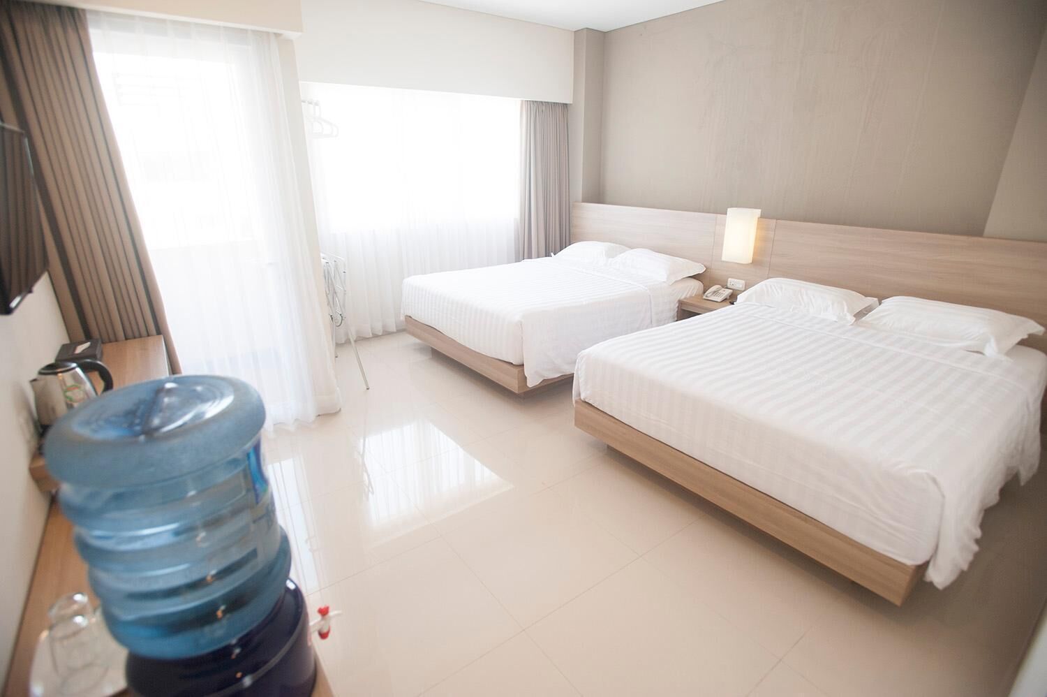A hotel room with two beds, a large water dispenser, and a bedside table with a lamp.