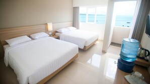 Ein Hotelzimmer mit zwei Betten, einem Nachttisch, einem Wasserspender und Blick aufs Meer.