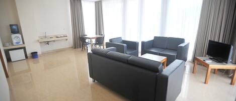 A modern living room with a sofa, two armchairs, a coffee table, a TV, and a dining area with a table and chairs.
