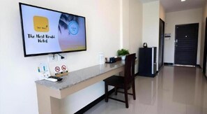Una mesa de recepción de hotel con un televisor de pantalla plana mostrando 'The Nest Krabi Hotel' y un cartel de 'SHA'.