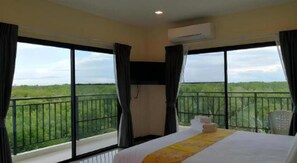 A hotel room with a large bed, a TV, and a balcony with a view of greenery.