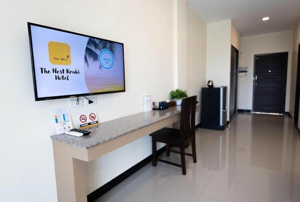 A reception area with a flat-screen TV displaying 'The Nest Krabi Hotel' logo, a reception desk, a chair, and a plant. - The Nest Residence (Krabi)
