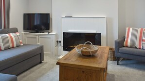Un saló amb televisió de pantalla plana, una llar de foc i dos sofàs amb coixins a ratlles.
