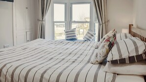 Un dormitori amb un llit gran, roba de llit a ratlles i una vista per una finestra amb cortines.