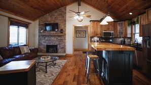 A cozy living room with a fireplace, a wooden ceiling, and a kitchen area with a bar. - Lakefront Cabin with Hot Tub! (Brookport)