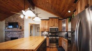 A kitchen with wooden cabinets, a granite countertop, a stainless steel refrigerator, a microwave, an oven, and a ceiling fan. - Lakefront Cabin with Hot Tub! (Brookport)