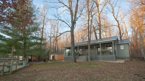 A cabin with a porch, surrounded by trees and a fenced area. - Lakefront Cabin with Hot Tub! (Brookport)