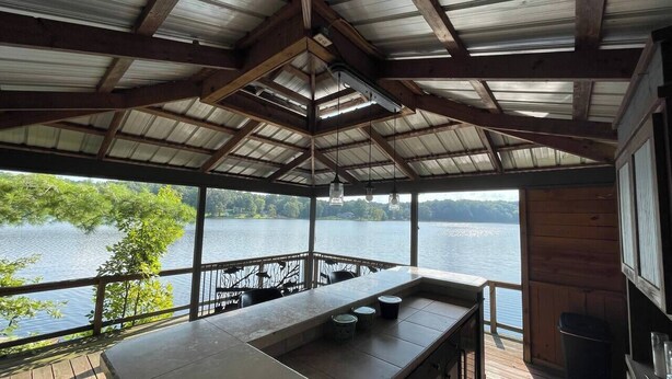 A covered outdoor deck with a bar area, overlooking a lake. - Lakefront Cabin with Hot Tub! (Brookport)