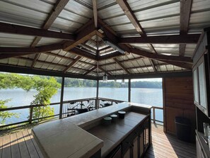 Terraza exterior techada con zona de bar, con vista a un lago.