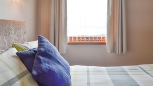 Ein Schlafzimmer mit einem Bett, Kissen, einem Fenster mit Vorhängen und einer Wandleuchte.
