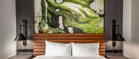 A modern hotel room with a large abstract painting on the wall, a wooden headboard, and two bedside tables with lamps.