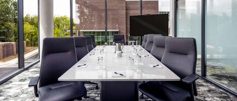 A conference room with a long table, black chairs, and a large screen.