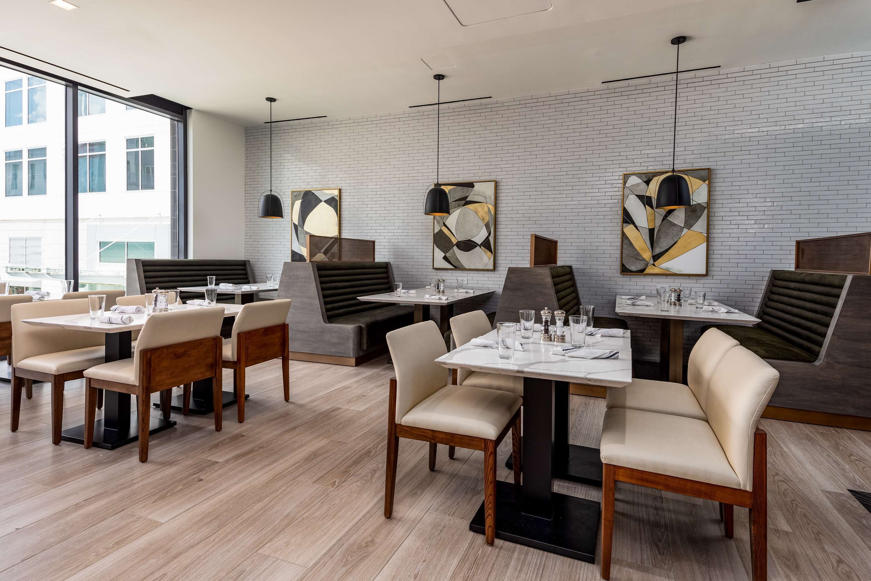 Un intérieur de restaurant moderne avec des tables et des chaises hautes, des œuvres d’art abstraites accrochées aux murs et une vue dégagée grâce à de grandes fenêtres.