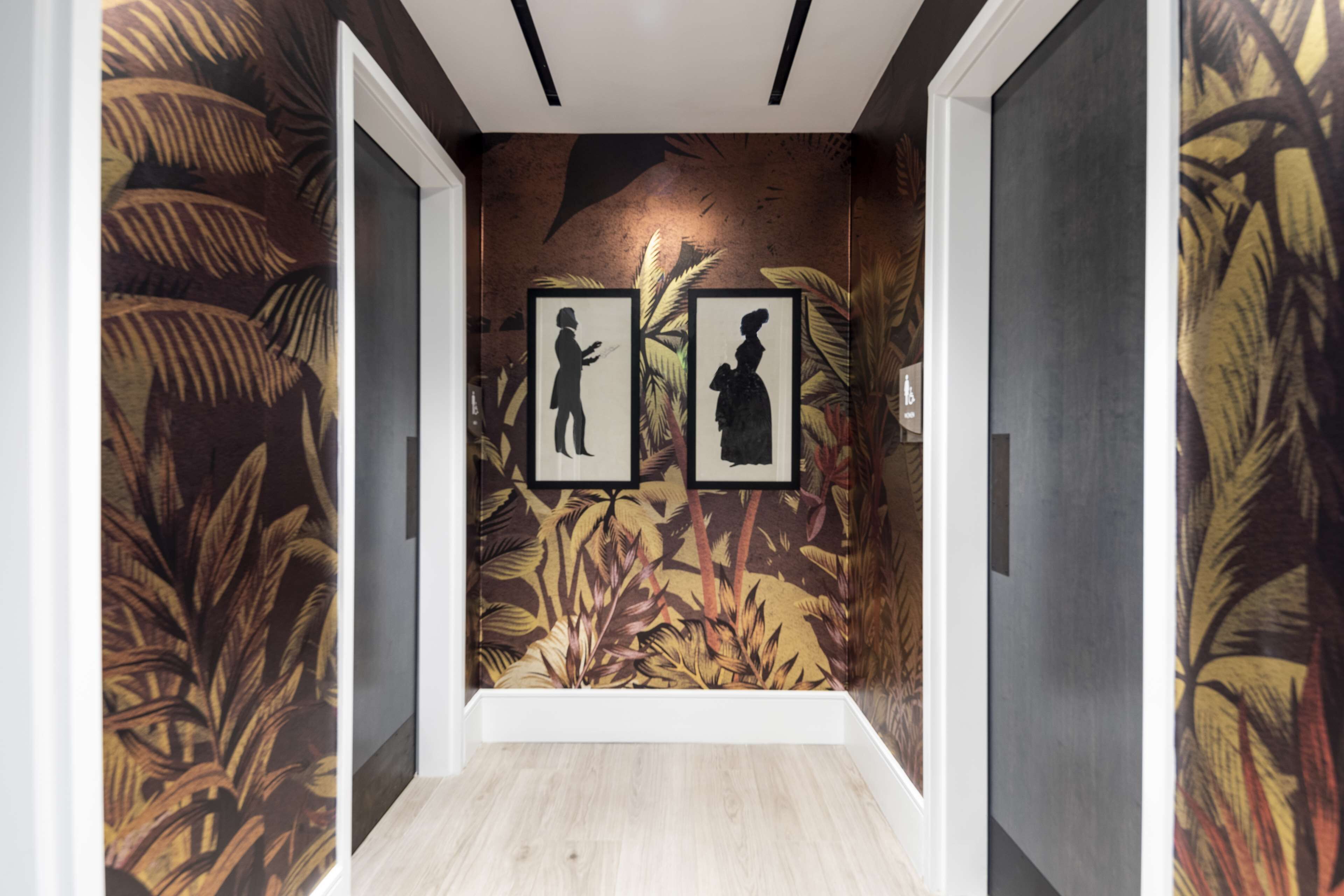 A hallway with a tropical mural, framed pictures, and wooden flooring.