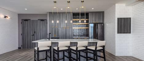 A modern kitchen with a central island, bar stools, pendant lighting, and a built-in wine rack.