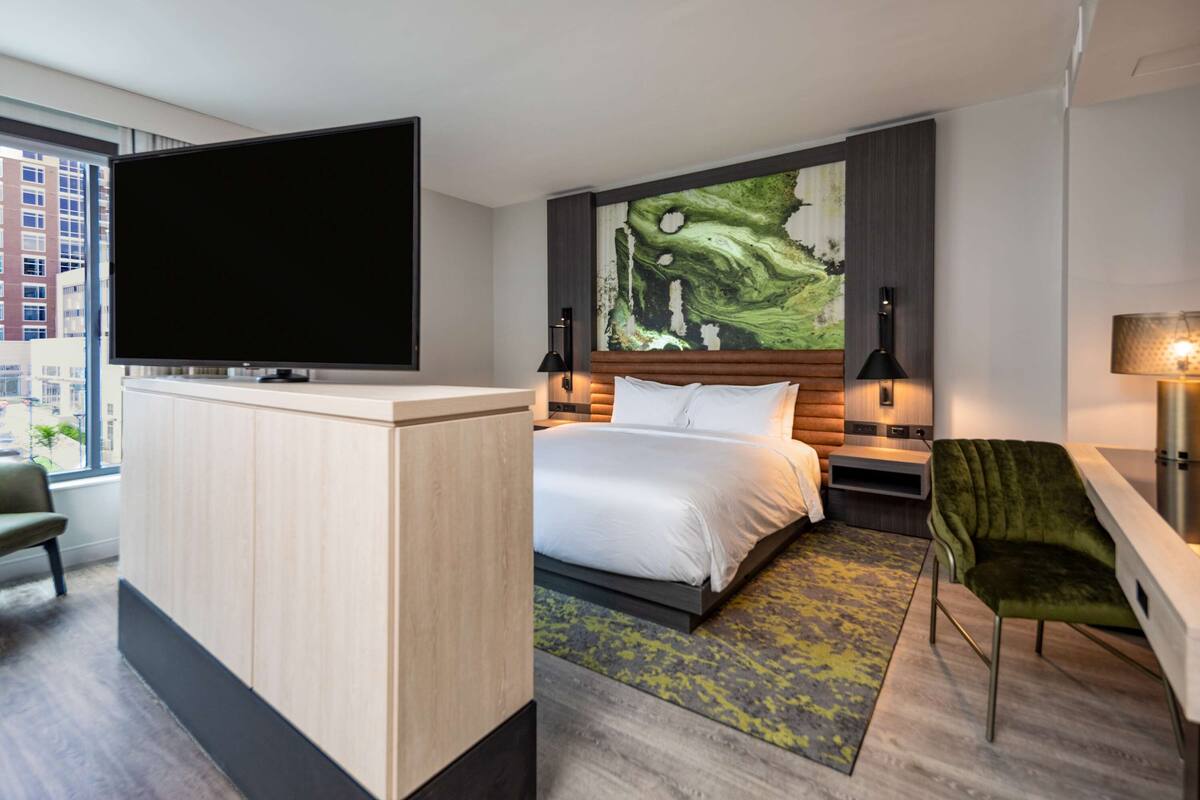 A hotel room with a bed, a TV, a desk, and a chair.
