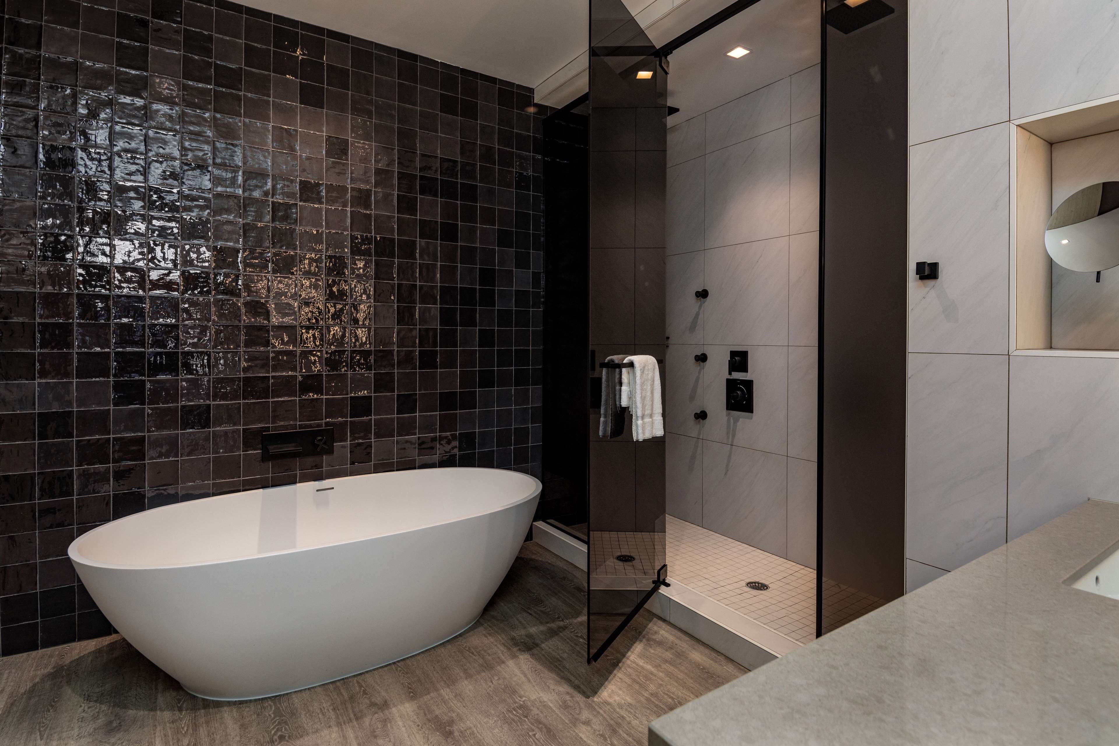 Een moderne badkamer met een vrijstaand bad, donkere betegelde wanden en een douchecabine met glazen wanden.