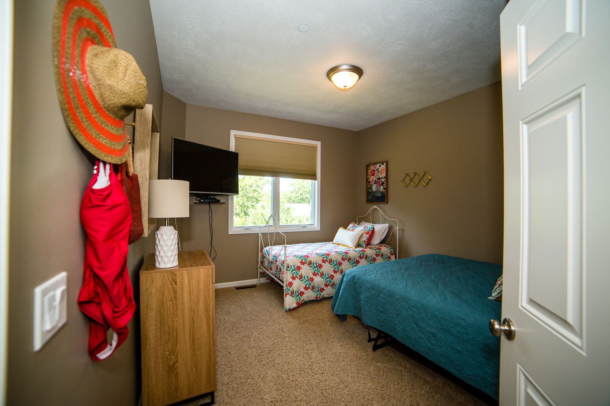 A bedroom with two beds, a TV, a window, and a door.