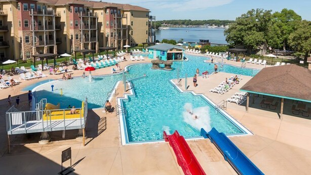 A swimming pool area with multiple slides, lounge chairs, and a view of a lake.