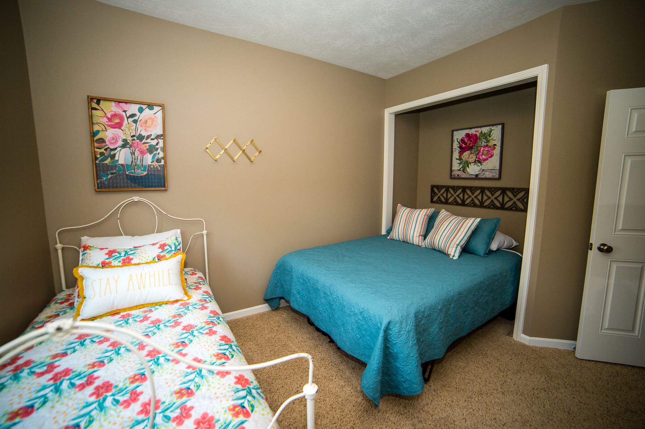 A bedroom with a bed, a nightstand, a door, and two wall-mounted paintings.