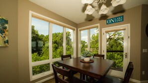 A dining area with a large table and chairs, large windows with a view of trees, and a sign on the wall that reads "ON LAKE TIME".