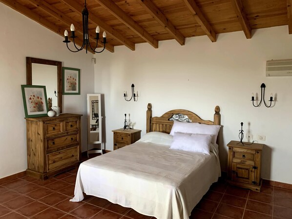 A bedroom with a wooden ceiling, a large bed with white bedding, two bedside tables with lamps, and a wooden dresser. - Villa Ensueño: a natural setting, a family-friendly environment (Barrio Taucho)