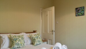 Una cama bien hecha con sábanas blancas y toallas enrolladas, un cabecero de madera y una puerta con picaporte.
