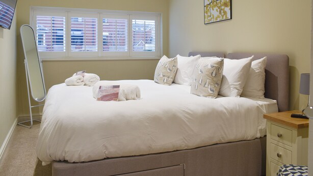 Una cama bien hecha con almohadas, una mesita de noche, una lámpara y una ventana con persianas.