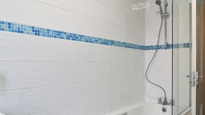 Un baño con azulejos blancos, un borde azulado y una bañera, ducha y lavamanos.