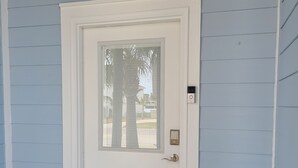 Una porta bianca con un'insegna che recita 'Beach Bungalow', una finestra con persiane, un campanello e un tappetino di benvenuto.