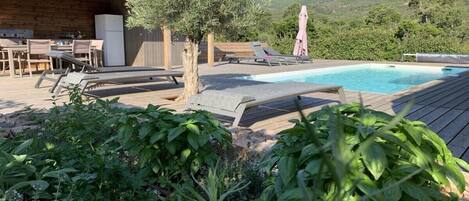 A wooden deck with a pool, lounge chairs, and a table with chairs.