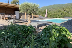 Um deck de madeira com piscina, espreguiçadeiras e uma mesa com cadeiras.