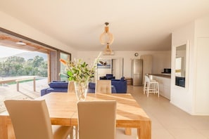 Sala de estar moderna com mesa de jantar de madeira, sofás azuis e uma grande janela com vista para o exterior.