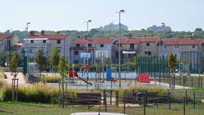 Un parc infantil amb diverses estructures de joc, envoltat per una tanca, i edificis residencials al fons.
