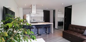 A modern kitchen with a central island, bar stools, and a brown leather sofa.