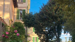 Ein Steinweg führt zu einem Gebäude mit grünen Fensterläden und einem Balkon.